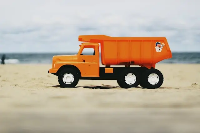 picture of a orange toy dump truck on a sandy beach